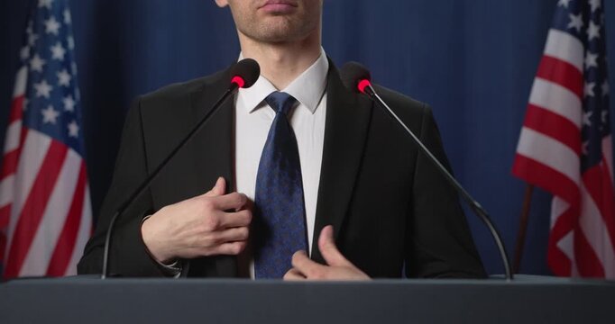 Man adjusts tie and suit behind podium with American flags
