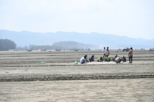 Cox's Bazar District, Bangladesh - 14 September 2026: View of people working on the sandy shore of Teknaf Beach with traditional fishing boats and distant hills.