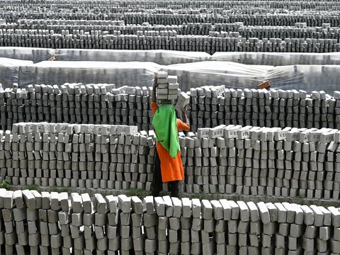 Dhaka, Bangladesh - 14 September 2026: View of a worker carrying a stack of bricks on their head at a brick kiln in Dhaka, with rows of drying bricks in the background.