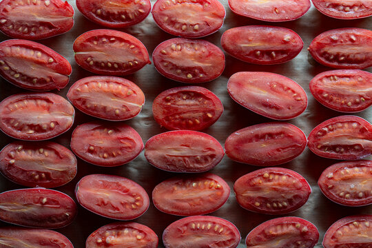 Top view of frozen plum tomato halves in row, closeup. Flat lay texture background of red plum tomatoes cut in half and frozen covered with white frost and ice crystals for winter food preservation