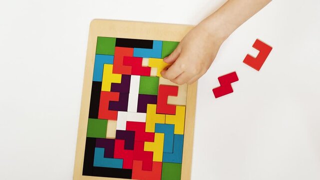4K slow motion 60 fps footage of a little child hand holding a red block while solving a bright colorful wooden logic puzzle game on a clean white desk.