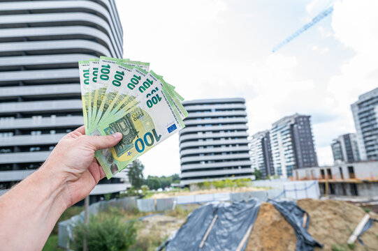 Male Hand Holding Stack of 100 Euro Banknotes Against Construction Site Building Exterior
