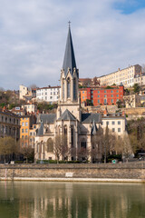 Obraz premium Historic church with spire overlooking a river and colorful buildings on a hill. Lyon