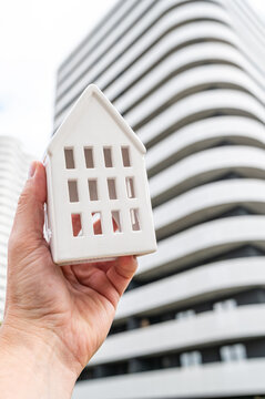 Vertical View of Hand Holding House Model Against Modern High Rise Residential Building Concept