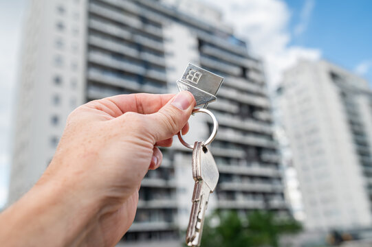 Hand Holding House Keys with Metal House Keychain in Front of High Rise Apartment Building Exterior