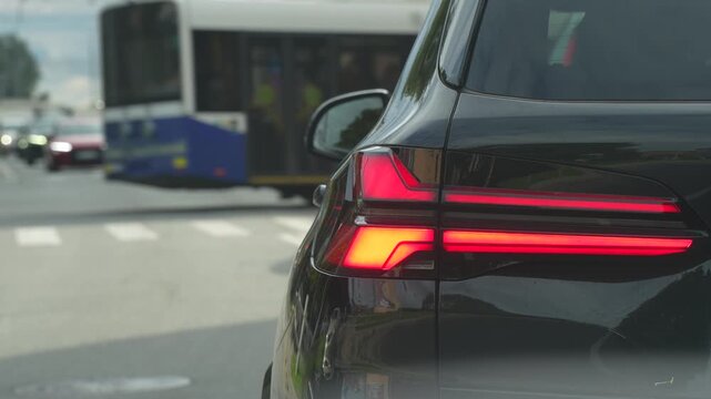 A car rear lamp assembly remains illuminated while vehicles cross a city intersection, showing automotive signaling within an active urban traffic network