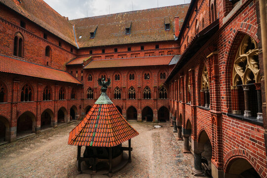 Malbork, Poland - 23 March 2026: View of the historic red brick courtyard and well house at Malbork Castle, featuring Gothic arches and intricate masonry.