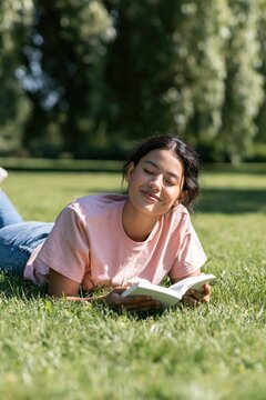 Young woman reading a book relaxing on grass in sunny park background for wellness lifestyle banner and mindful leisure design