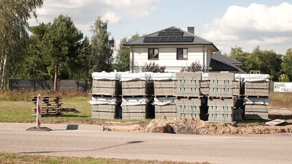 Materiały budowlane ułożone na paletach przed nowo wybudowanym domem jednorodzinnym z panelami fotowoltaicznymi na dachu. © tomo81