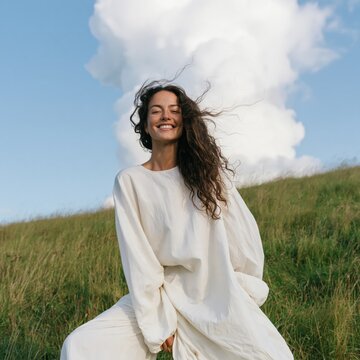 Smiling woman in flowing white dress on grassy hill for wellness background and nature lifestyle banner