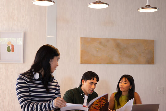 Collaborating at dining nook, Diverse coworkers reviewing colorful book, laptop, papers
