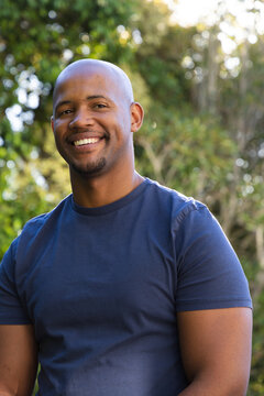 African man smiling and looking at camera outdoors in navy t-shirt with sunlit leaves bokeh