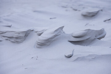 Obraz premium Wind-sculpted sand ridges are revealing layered overhangs on coastal dune, with scattered pebbles