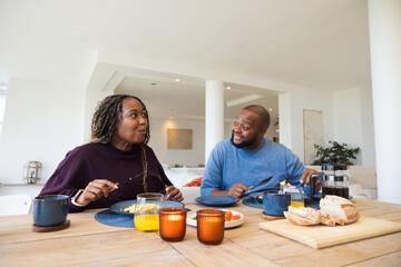 Obraz premium African American couple at home dining table in maroon blue sweaters sharing meal with French press
