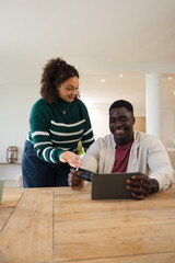 Obraz premium African American couple sitting at wooden table, man holding tablet with reader, woman handing card