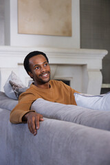 Obraz premium Adult male sitting in living room on gray sofa, wearing brown sweater, with throw pillows