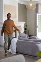 Obraz premium Adult male standing beside gray sectional sofa in living room, resting hand on throw