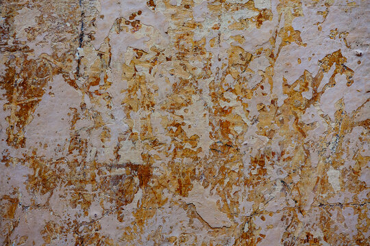 Grunge texture of old peeling plaster wall background. Closeup of weathered cracked stucco wall with multiple layers of peeling beige and brown paint, abstract vintage backdrop for design mockup