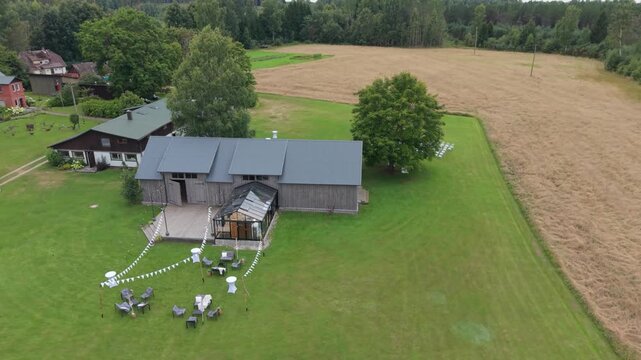 Aerial view of a rustic venue with a wooden building, green lawn, and rows of white chairs set up for an outdoor event in a serene countryside setting