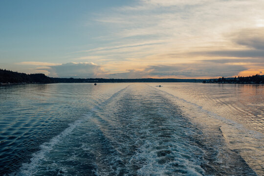 two boat trailing in wake of ferry boat after sunset