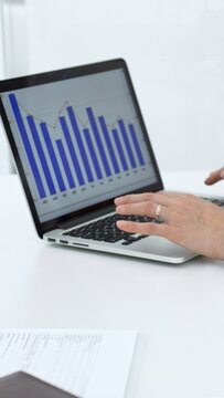 Businessperson analyzing financial charts on a laptop screen, typing on keyboard while reviewing data, working on reports for company growth, market strategy, and investment performance