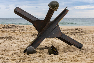 Background. Three American infantry helmets from World War II on the beach next to a czech hedgehog    © krysek