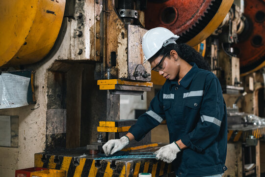 Industrial worker operating mechanical press in factory workshop with protective equipment and focused expression