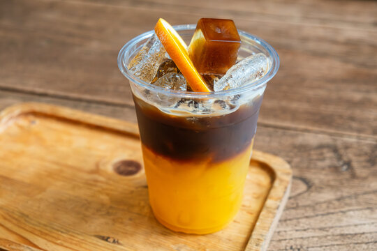 Cold Bumble coffee combining fresh orange juice and espresso with ice, orange slice and coffee ice cube, served on wooden tray in Thailand. Coffee recipe, specialty cafe menu, tropical refreshment