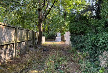 Obraz premium A quiet, tree lined path winds its way to a sunny clearing, with a wooden fence running along one side, adding a quaint rustic charm in Heaton, Bradford, Yorkshire, UK.