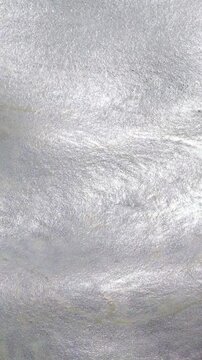 Nahaufnahme in Zeitlupe aus der Vogelperspektive: Wei&szlig;er Schaum treibt bei leichtem Wellengang auf einer Wasseroberfl&auml;che. Das nat&uuml;rliche Sonnenlicht spiegelt sich glitzernd in den Bl&auml;schen. 