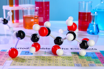 Chemical model of glucose molecule, periodic table and laboratory glassware on white table, closeup