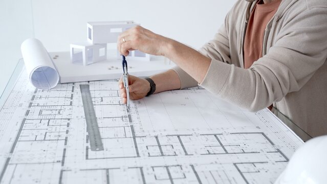 Architect working on a blueprint, using a compass to measure and draw lines for a new building project, creating architectural plans and construction designs with precision