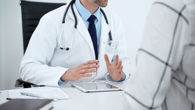 Doctor and patient having a medical consultation in a modern clinic, physician using a digital tablet for diagnosis and discussing healthcare with a woman