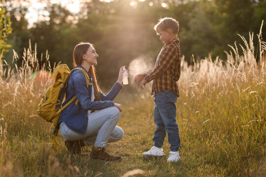 Mother spraying insect repellent onto her son's arm outdoors