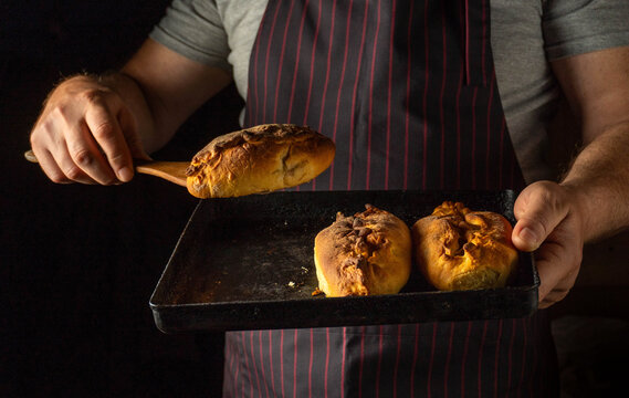Hands carefully lift freshly baked bread rolls from a dark pan, revealing their golden crust and inviting texture. The cozy kitchen atmosphere adds to the warmth