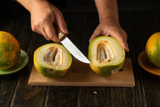 A person is skillfully slicing a bright melon in half, revealing its juicy flesh. Surrounding the scene are other melons and a warm, inviting kitchen atmosphere