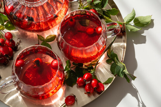 Rosehip tea served in glass cups and teapot on a metallic tray with fresh rosehips and leaves