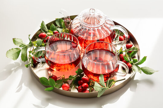 Crimson rosehip tea served in clear glass cups and teapot on silver tray with fresh branches