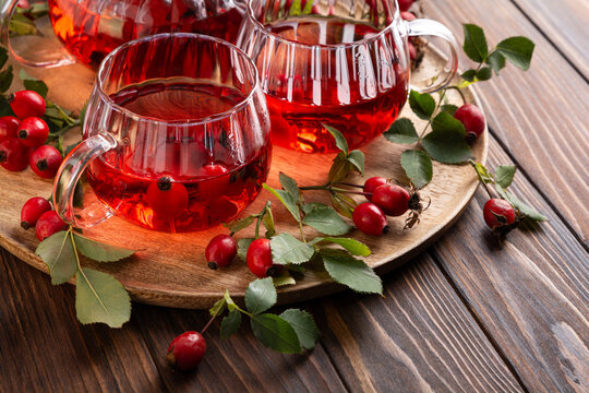 Rosehip tea served in clear glass cups with fresh rosehip berries on a wooden board