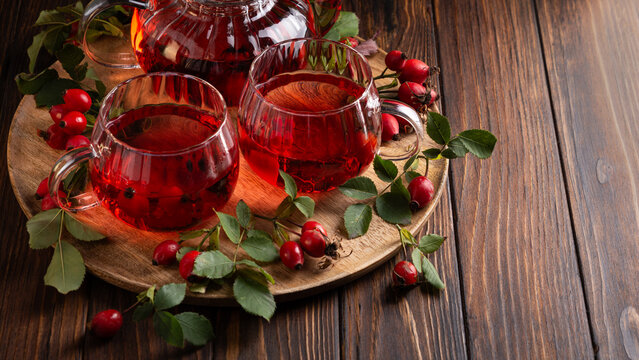 Warm Rosehip Tea Served in Glass Cups with Fresh Berries and Green Leaves on Wooden Surface
