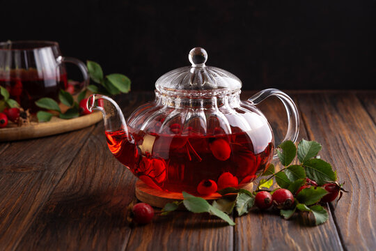Clear glass teapot filled with vibrant red rosehip tea and fresh berries on wooden table