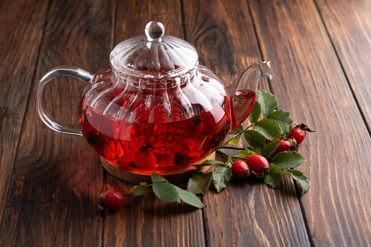 Glass teapot filled with brewed rosehip tea and fresh berries rests on wooden background
