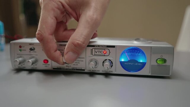 Professional music producer hand adjusting gain control on microphone preamplifier. Sound engineer working on audio interface, setting input level for recording, close-up, slow motion.