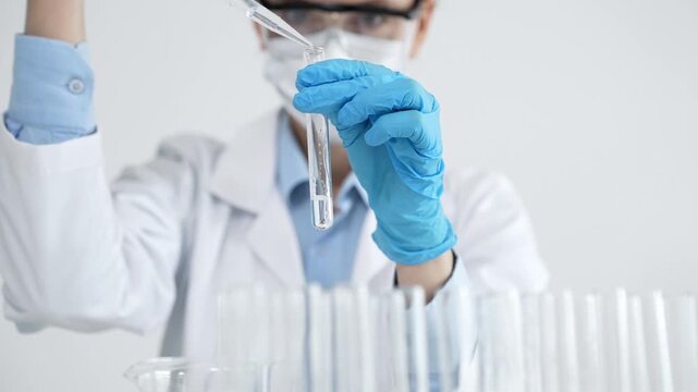 Scientist in protective gear performing a critical laboratory experiment, carefully transferring liquid with a pipette into a test tube during medical research and development