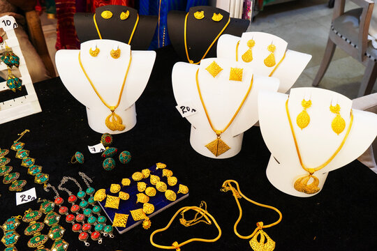 A high-angle showcase of elegant gold jewelry sets displayed on white and black neck busts. The collection features intricate filigree necklaces with large patterned pendants and matching earrings
