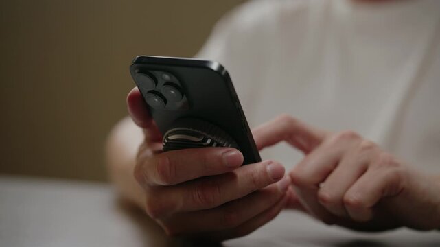 Unrecognizable person using smartphone equipped with magnetic power bank and grip, scrolling through content with finger, concept of portable energy and convenient handling, close-up, slow motion.