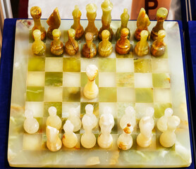 A top-angle shot showcasing a beautiful collectible chess set meticulously crafted from natural polished onyx marble stone. The semi-translucent figures are arranged on a matching checkered board with © Orkhan