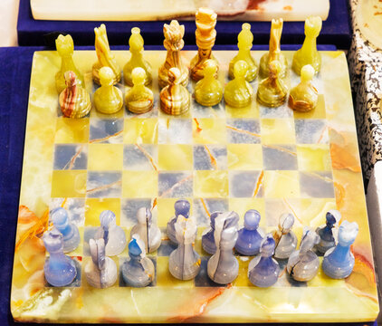 A top-angle close-up shot of a luxurious handcrafted chess set made from premium natural onyx stone. The semi-translucent chess pieces are arranged in their starting positions on a glossy checkered