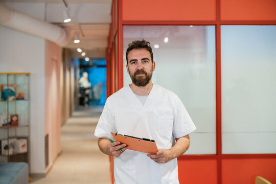 Male doctor holding clipboard standing in clinic