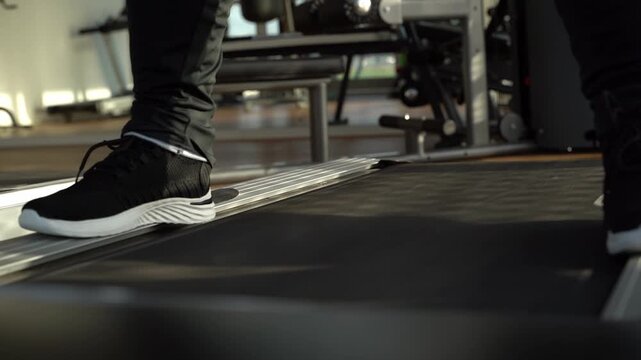 Feet step firmly on treadmill surface. Movement suggests active, focused workout routine. Athlete wears black athletic shoes and matching pants. Low angle emphasizes treadmill mechanics and stride